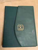 Closed green folder style book with Royal Canadian Mint gold emblem on cover.