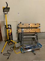 Photo showing Black & Decker folding work bench, one halogen work light on tripod stand, second halogen work light on floor, a mitre box with saw on floor in front of work bench.