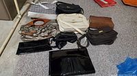Nine assorted purses, clutches, and handbags arranged on light carpet floor, showing variety of styles and colors.