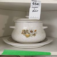 Tureen with lid and matching plate, beige speckled with floral and fruit design, showing side and frontal views.