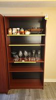 Front view of the bookcase showing five shelves with some glassware and small items on two shelves, with yellow tape on shelf edges.