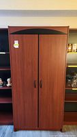Front view of closed wooden cupboard with two doors and black handles.