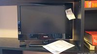 Haier 19 inch LED TV with glossy black bezel and Haier logo below screen, showing TV placed on a shelf with a manual and remote.