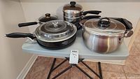 Full view of all pots, pans, and baking dishes included in the lot on a small folding table.