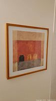 Framed square print on wall with abstract geometric shapes in muted colors in a light wooden frame.