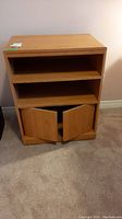 Front view of wooden cabinet with two shelves and lower cabinet doors slightly open.