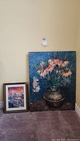 Framed print of Fisherman's Wharf with boats and sunset on the left; large Vincent floral poster on the right, sitting on carpeted floor against wall.