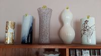 Five assorted flower vases displayed in a row on a wooden shelf, showing different shapes and styles.