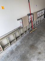 Full view of the 20-foot ladder leaning against a wall with two small mats and a push broom in front of it