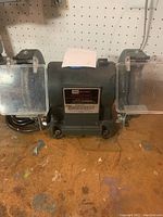 Front view of bench grinder showing overall condition, grinding wheels, and clear plastic eye shields.