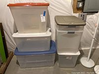 Photo showing six stacked plastic storage bins with different colored lids against a plain background.
