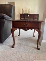 Front view of one end table showing drawer with decorative metal pulls and cabriole legs.