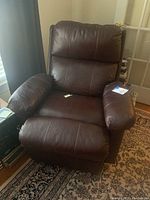 Front view of brown leather recliner chair showing cushioned padded arms, seat, and backrest with visible seam stitching.