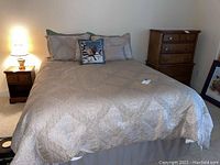 Fully assembled queen bed with comforter, pillows, nightstand and dresser visible
