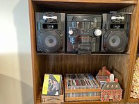 Full view of RCA sound system with 5 CD changer and two speakers on wood shelf alongside crates filled with CDs.