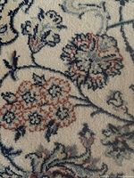 Close-up of the rug's floral pattern showing rust, navy, and grey embroidery details on a cream background.