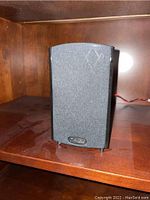 Single vertical Definitive Technology black speaker with fabric grille on a wooden shelf