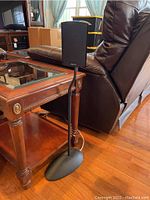 Definitive Technology surround sound speaker mounted on a black stand next to furniture.