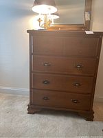 Front view of the brown wooden dresser showing six drawers with metal handles and bracket feet.