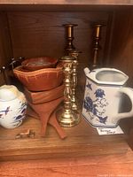 Wooden serving dishes, brass candlesticks, porcelain tea pot and cheese cutter arranged on a shelf