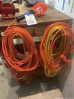 Photo showing hanging orange cage work light and two long coiled extension cords, one orange and one yellow with orange stripes.