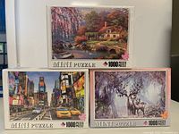 Box set of three sealed 1000 piece mini puzzles with different scenic artwork.