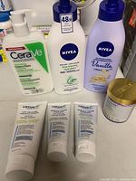 Seven assorted facial and body lotions, cleansers, and creams from CeraVe, Nivea, Lotus Aroma, and Truly shown together on a surface.