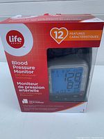 Photo of boxed Life brand blood pressure monitor showing branding, 12 features, Bluetooth technology, and product image.