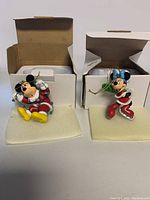 Two ornaments in original white boxes, Mickey on the left sitting with lights, Minnie on the right skating.