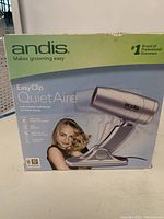 Box showing brand Andis Easy Clip QuietAire dog dryer with image of handheld dryer and person holding small dog.