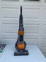 Front view of upright vacuum showing handle, dust bin, base and hose