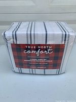 Photo of packaged True North Comfort flannel sheet set, shows brand and product details on label with red and black plaid design.