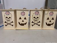 Front view showing four wooden Halloween lanterns with cut-out skull and jack-o'-lantern faces, unpainted and brand new.