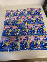 21 unopened LEGO DOTS Extra Dots Series 6 packs laid out on a white surface in 3 rows, 7 packs each, showing consistent packaging with colorful designs featuring alien and emoticon graphics.