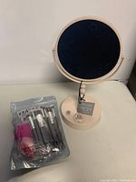 Light pink magnifying mirror on stand next to packaged makeup brushes and sponges.