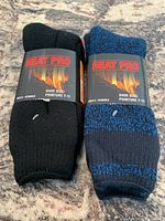Two pairs of Heat Pro men's thermal socks, one in black and one in blue heather, each with packaging showing shoe size 7-11