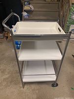 Front view of the 3-level utility cart showing metal frame with white plastic tray on top, and two shelves below.
