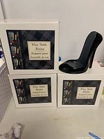 Three white boxes stacked, each labeled 'Wine Bottle Holder' with a picture of the black high heel shaped holder on the box. One holder displayed next to the boxes.