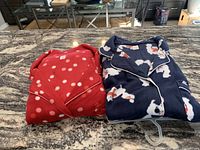 Two folded fleece pajama sets on countertop: pink with white polka dots, navy blue with white cats.