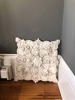 Front view of the large square resin wall plaque against a gray wall and white baseboard on wood floor.