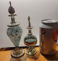 Photo showing two hand blown blue glass perfume bottles with gold accents beside a soda can for size comparison.