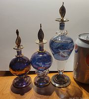 Photo of three hand blown blue glass perfume bottles with gold detailing, varying heights, placed next to a soda can for size reference.