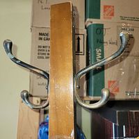 Close up image of a wood panel from the coat rack showing two sets of vintage metal hooks with curved ends, attached to the wooden post which shows visible scratches.