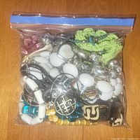 Photo of one sealed zip-top bag filled with mixed costume jewelry beads in white, green, blue, yellow, pink, and silver tones