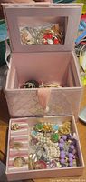 Pink quilted jewelry box with mirror and assorted costume jewelry inside, viewed from above.