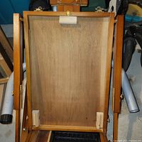 View of the inside of the easel tray with wooden frame and backing showing storage compartments.