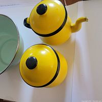 Yellow enamelware teapot and covered dish with black knobs and handle viewed from side and top.