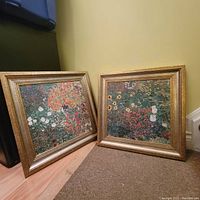 Two matching framed floral garden paintings leaning against a wall on the floor, showing both paintings side-by-side.