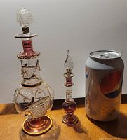 Two hand blown Egyptian perfume bottles next to a soda can for size reference, showing detailed glasswork and stoppers.