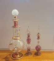 Three hand blown Egyptian perfume bottles with gold and purple decorative elements against neutral background.